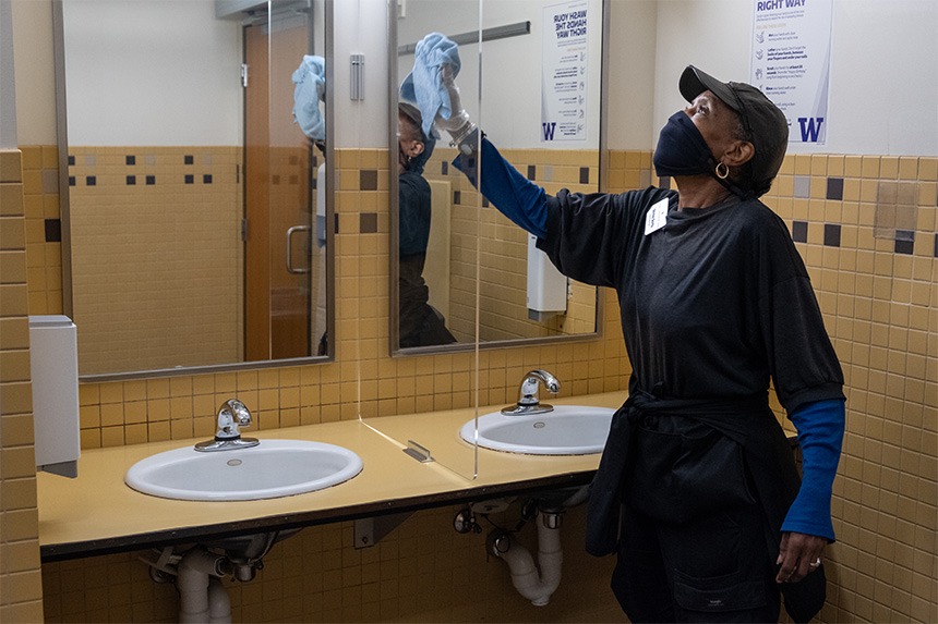 Custodian Shirley Dority cleans a Plexiglas shield between two sinks in a UW Tacoma bathroom.