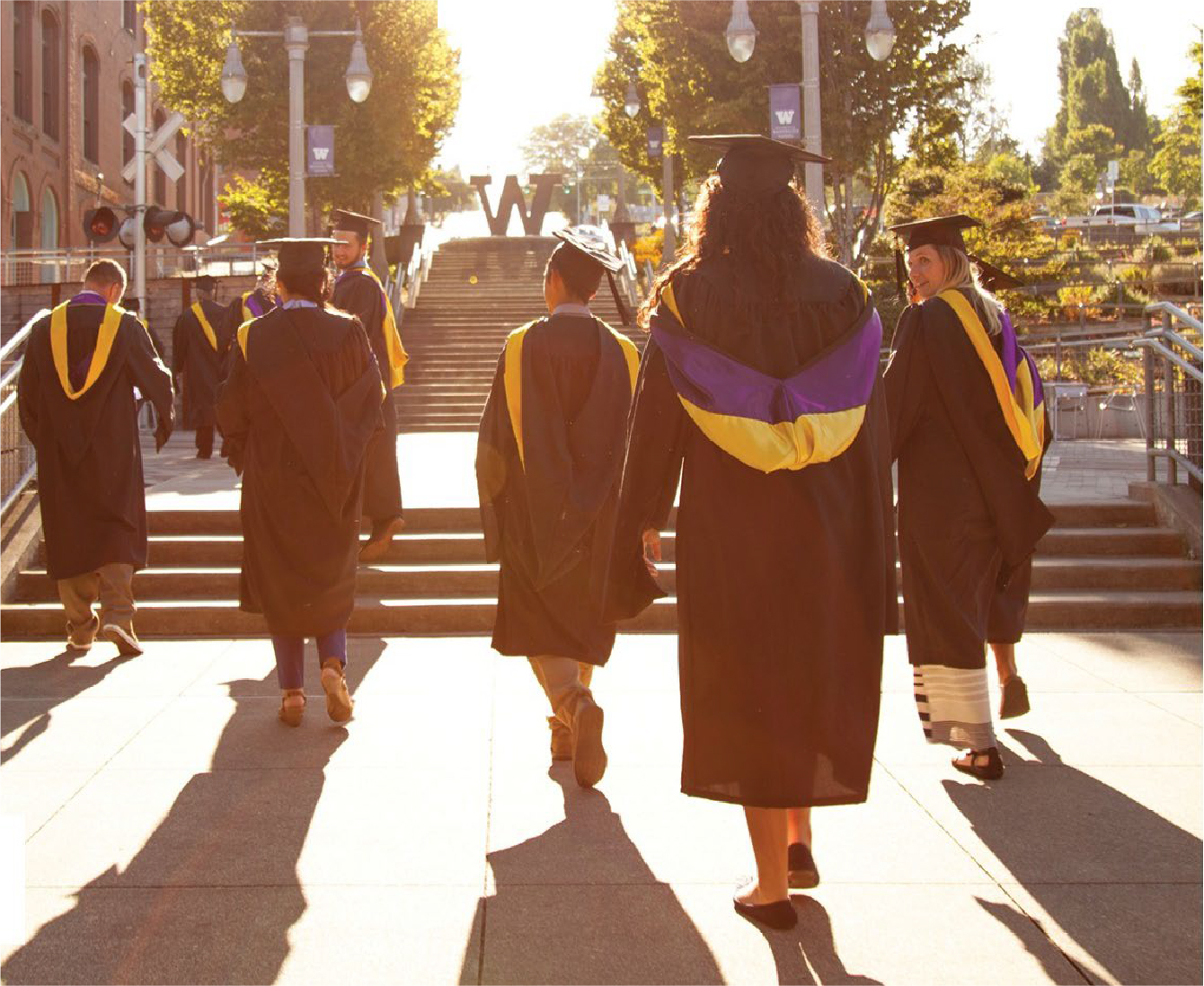 several graduating students walking up the stairs towards the W sign on the UW Tacoma campus