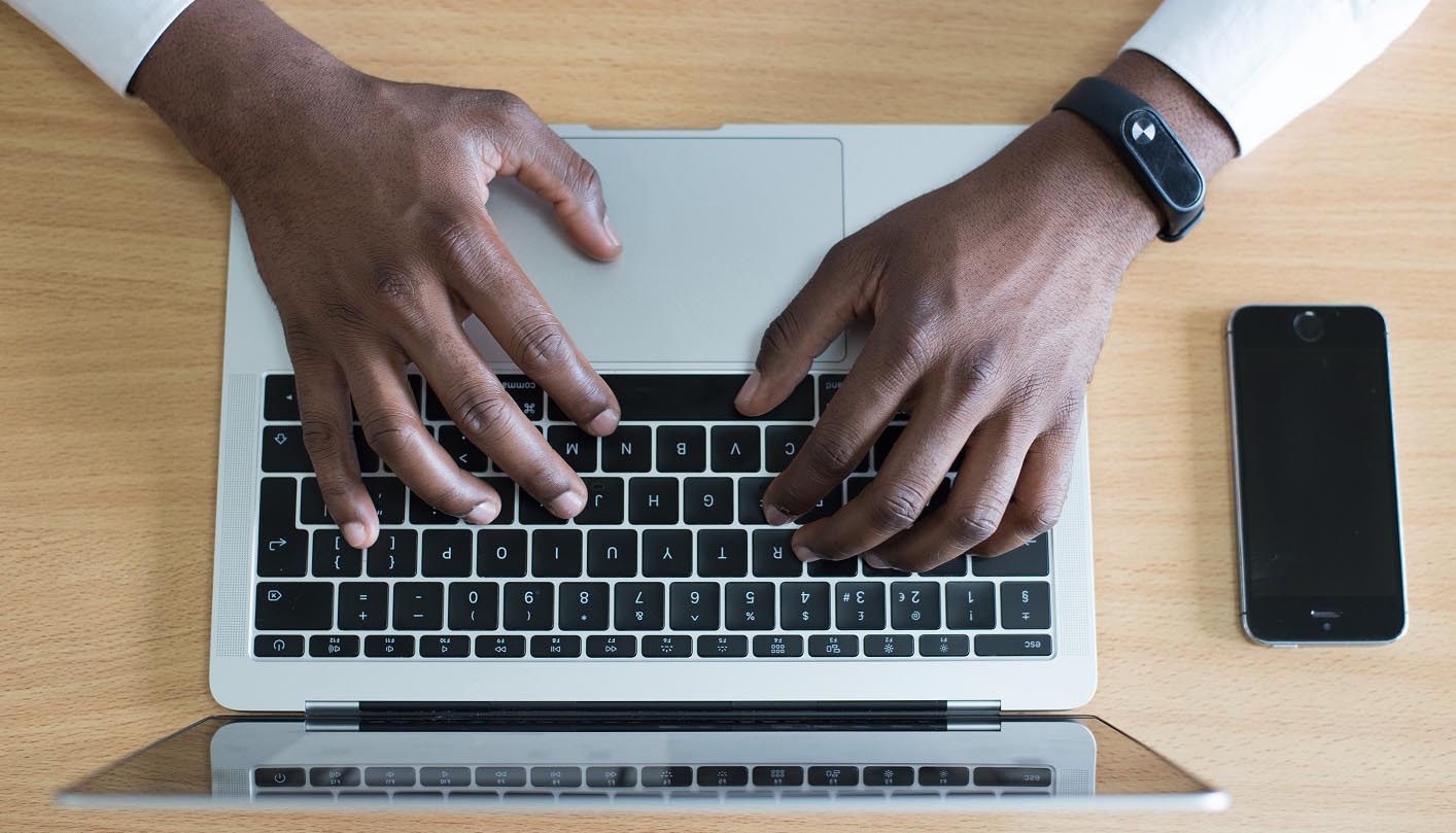 Dark-skinned hands typing on a laptop