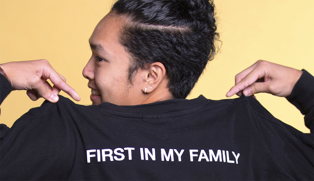 Photo of student looking backwards holding up shirt that says "First in my family"