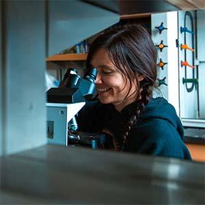 UW Tacoma environmental sciences student Hozoji Matheson-Margullis looking through microscope eyepiece.