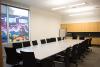 Community room with three square tables put together in one large table with 20 black, wheeled chairs around