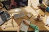 person taking notes in a paper notebook while watching a video call on a computer monitor