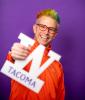 Alex Zerbe, wearing orange jacket, with rainbow-colored hair, holding W Tacoma prop.