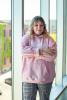 Hana Mei, a student employee, stands inside by large glass windows, wearing a pink University of Washington sweatshirt.