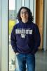 Trevor stands inside, in front of large glass windows, wearing a purple University of Washington sweatshirt.