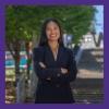 a photo of Kalea Velasco-Cosare. She is standing on the grand staircase on the UW Tacoma campus. She is wearing a black blazer and she has her arms crossed in front of her chest.