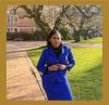 a photo of Salese Clark. She has shoulder length black hair and is wearing a blue skirt suit and blazer. She is standing on a brick path in front of a tree.