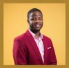 a photo of Simon Njoroge. He is wearing a light pink shirt under a red suit coat. He is standing in front of a gold background.