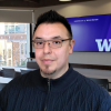 Man in dark hair and glasses stands in a classroom with the University of Washington logo on a display screen behind him.